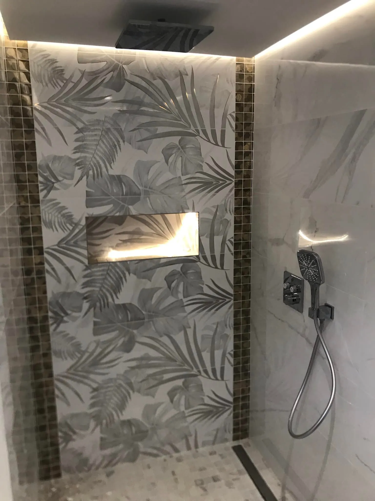 Douche à l'italienne avec carrelage à motif feuillage, niche éclairée et colonne de douche noire