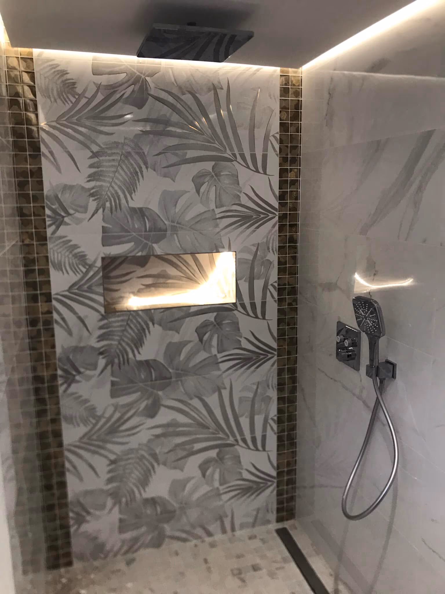 Douche à l'italienne avec carrelage à motif feuillage, niche éclairée et colonne de douche noire