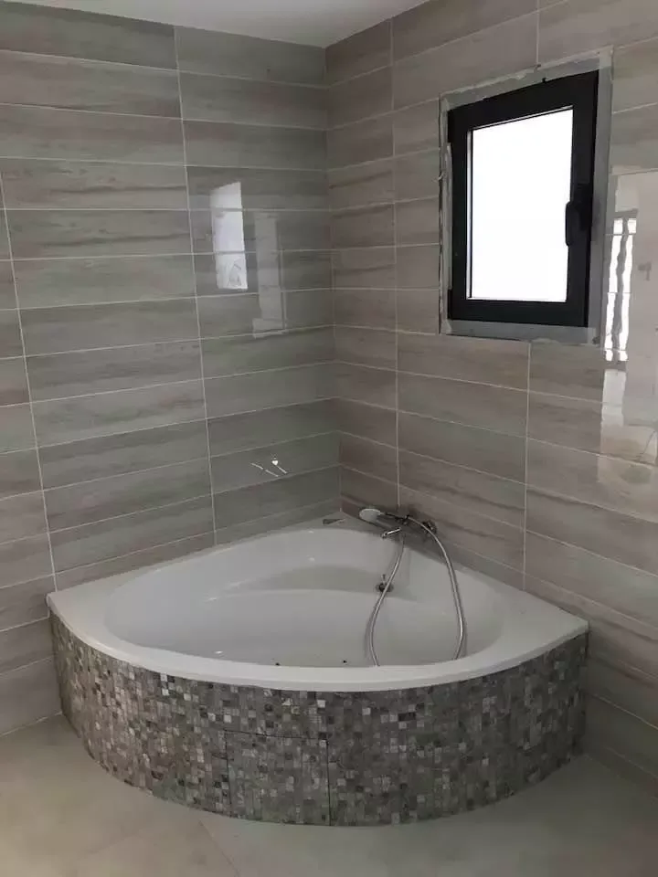 Baignoire d'angle carrelée sous une fenêtre