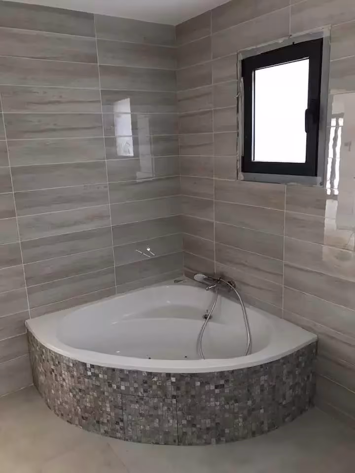 Baignoire d'angle carrelée sous une fenêtre