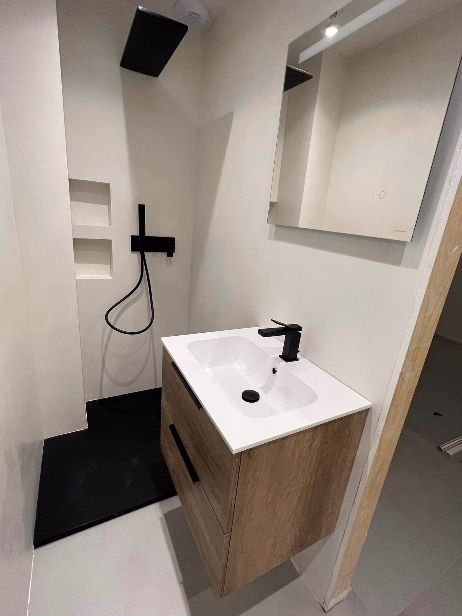 Salle de bain blanche avec meuble vasque en bois, robinetterie noire et receveur de douche noir