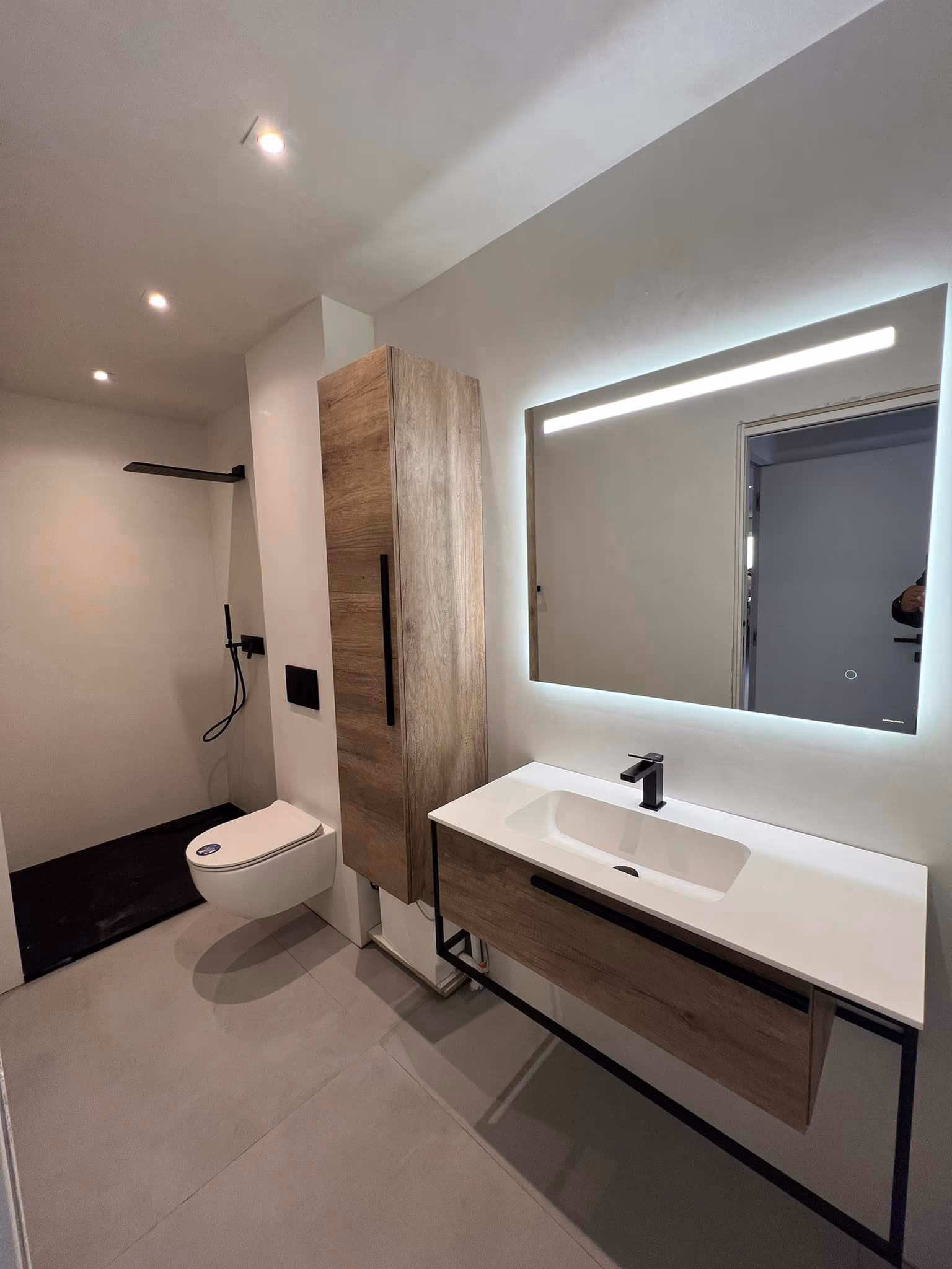 Salle de bain avec miroir éclairé, meuble vasque suspendu en bois et colonne de rangement