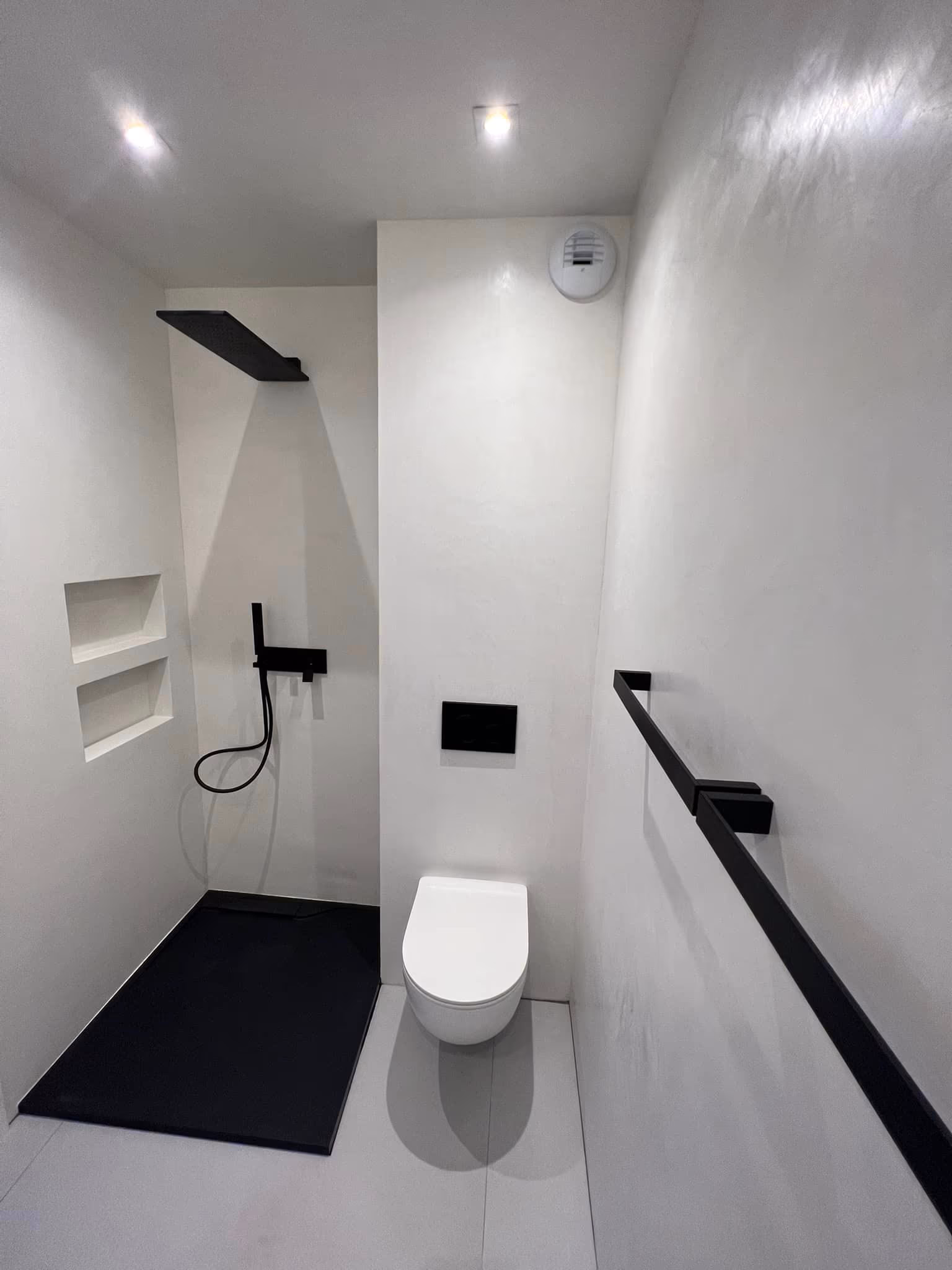 Salle d'eau blanche avec douche à receveur noir, niches murales, WC suspendu et barre murale noire