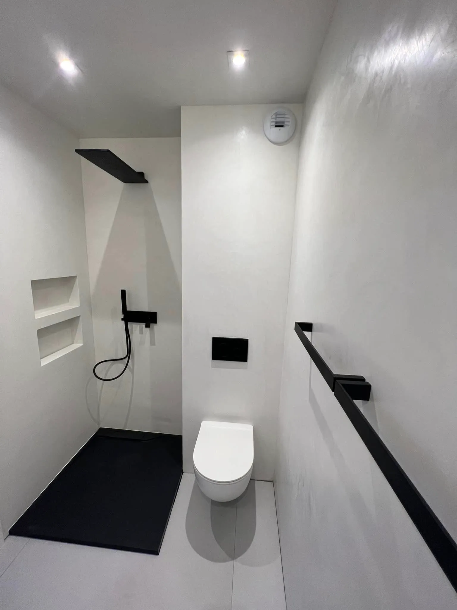 Salle d'eau blanche avec douche à receveur noir, niches murales, WC suspendu et barre murale noire